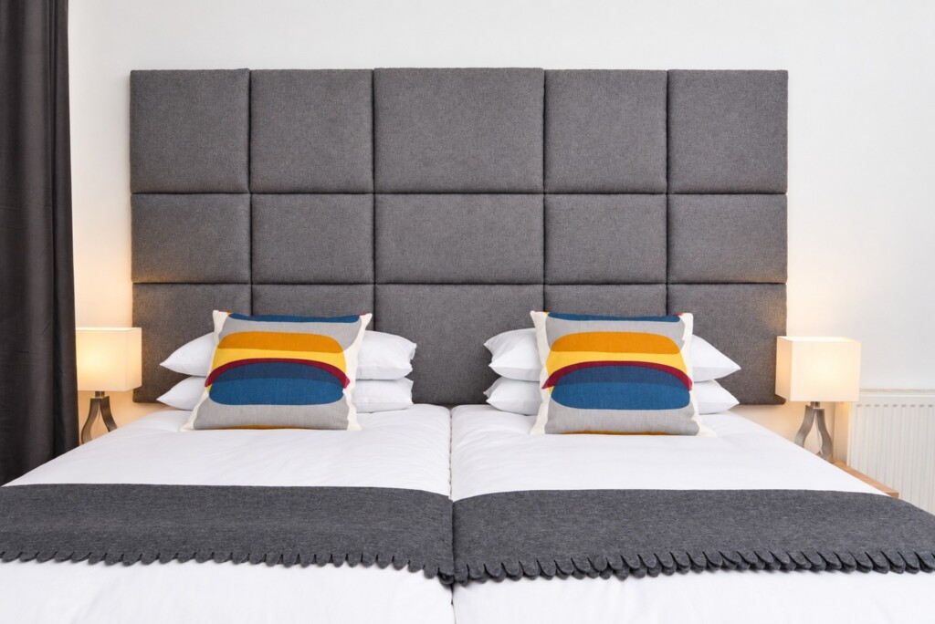 Beds arranged together beneath a grey upholstered headboard at Baxter Park City Base, a two-bedroom apartment in Dundee.