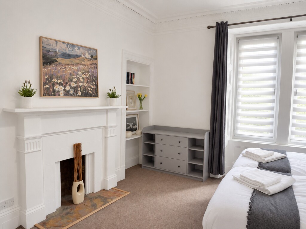 White bedroom fireplace beneath artwork, recessed shelves and a grey storage unit with three drawers and open side shelves.