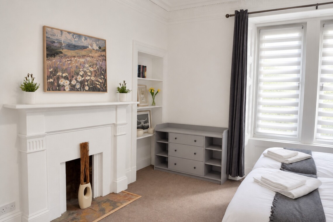 White bedroom fireplace beneath artwork, recessed shelves and a grey storage unit with three drawers and open side shelves.