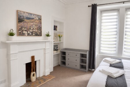White bedroom fireplace beneath artwork, recessed shelves and a grey storage unit with three drawers and open side shelves.
