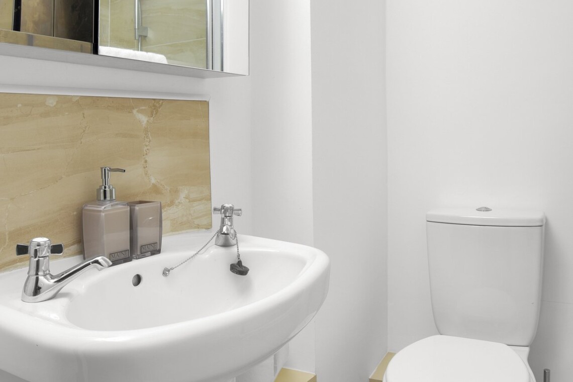 White pedestal basin beneath a mirrored cabinet, with a toilet alongside and beige tiles behind the basin.